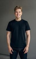 A portrait of a man in a black t-shirt and jeans, standing against a neutral grey background. photo