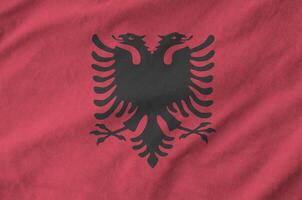 Albania flag depicted on folded wavy fabric of old cloth photo