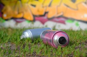 Several used spray cans with paint and caps for spraying paint under pressure on grass near the painted wall in colored graffiti photo