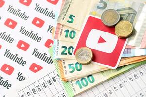 KYIV, UKRAINE - APRIL 20, 2024 YouTube logo and many euro money bills. Symbol of famous social network platform and european currency banknotes photo