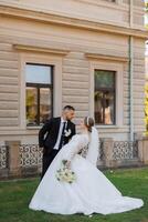 A bride and groom are posing for a picture in front of a building. The bride is wearing a white dress and the groom is wearing a suit. Scene is happy and celebratory, as the couple is getting married photo
