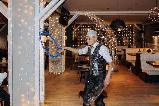 A man in a suit is blowing bubbles in a restaurant. The bubbles are blue and are floating in the air. The scene is lively and fun, with the bubbles adding a playful touch to the atmosphere photo