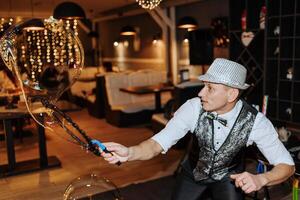 A man in a hat and vest is blowing bubbles. The bubbles are floating in the air and the man is holding a wand. The scene is lively and fun, with the bubbles adding a playful touch to the atmosphere photo