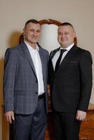 Two men in suits are posing for a picture. One of them is wearing a tie. Scene is formal and professional photo