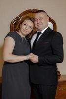 A man and woman are standing in front of a mirror, smiling at the camera. The man is wearing a suit and tie, while the woman is wearing a dress. Scene is happy and romantic photo