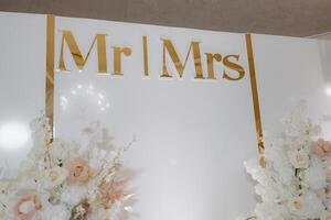 A white wall with gold lettering ,wall is decorated with flowers and has a gold border photo