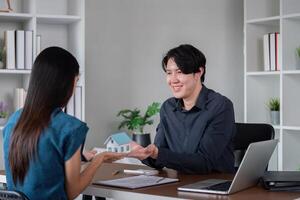 Real Estate Agent Showing Model House to Client in Modern Office Setting with Laptop and Documents photo