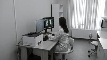 Female doctor looks at X-ray on computer. Clip. Doctor in bathrobe looks at tests and X-rays in computer room. Modern electronic technologies in medical clinics photo