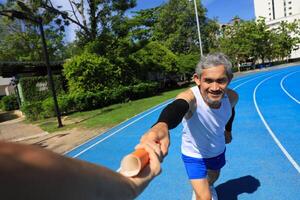 Senior Asian athlete is practicing running with relay baton in the professional blue track for professional exercise, sport training workout and healthy for longevity concept photo