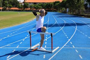 Senior Asian athlete is practicing hurdling running in the professional blue track for professional exercise, sport training workout and healthy for longevity concept photo