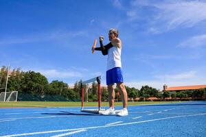Senior Asian athlete is practicing hurdling running in the professional blue track for professional exercise, sport training workout and healthy for longevity concept photo