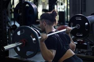 Caucasian muscular body builder sport man is practice weight training on squat barbell for core muscle inside gym with dark background for exercising and workout photo