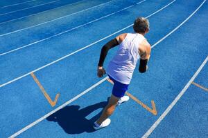 Senior Asian athlete is practicing running with relay baton in the professional blue track for professional exercise, sport training workout and healthy for longevity photo