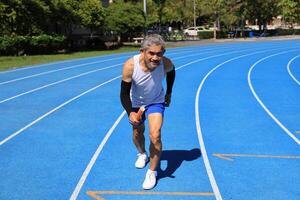 Senior Asian athlete is practicing running with relay baton in the professional blue track for professional exercise, sport training workout and healthy for longevity concept photo