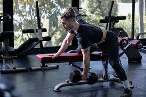 Caucasian man with strong and muscular body training on bent over row dumbbell with bench to build back and wing muscle inside the gym photo