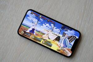 Fate Grand Order mobile iOS game on iPhone 15 smartphone screen on wooden table during mobile gameplay photo