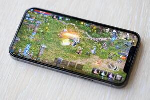 Lineage M mobile iOS game on iPhone 15 smartphone screen on wooden table during mobile gameplay photo