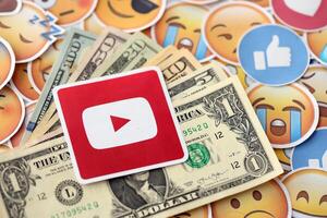 KYIV, UKRAINE - APRIL 20, 2024 YouTube logo and many usd money bills. Symbol of famous social network platform and dollar currency banknotes on lot of emoji reactions photo
