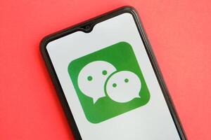 KYIV, UKRAINE - APRIL 1, 2024 Wechat or Weixin icon on smartphone screen on red table photo