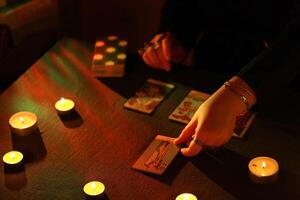 KYIV, UKRAINE - JULY 10, 2024 Tarot reader picking tarot cards. Candlelight in dark room. Tarot reader or fortune teller reading and forecasting photo