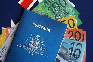 KYIV, UKRAINE - JULY 10, 2024 Australian blue travel passport and money bills on Australia flag background photo