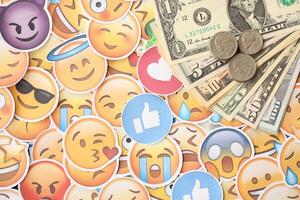 KYIV, UKRAINE - APRIL 20, 2024 USD dollars money and large set of stickers with Emoji yellow faces. The concept of smm, smo paid service for boost in social media photo