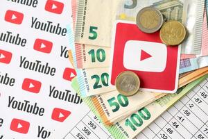 KYIV, UKRAINE - APRIL 20, 2024 YouTube logo and many euro money bills. Symbol of famous social network platform and european currency banknotes photo