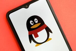 KYIV, UKRAINE - APRIL 1, 2024 Tencent QQ icon on smartphone screen on red table photo