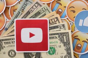KYIV, UKRAINE - APRIL 20, 2024 YouTube logo and many usd money bills. Symbol of famous social network platform and dollar currency banknotes on lot of emoji reactions photo