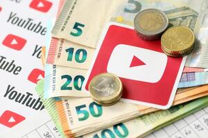 KYIV, UKRAINE - APRIL 20, 2024 YouTube logo and many euro money bills. Symbol of famous social network platform and european currency banknotes photo