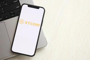KYIV, UKRAINE - MARCH 15, 2024 XTcom logo on iPhone display screen on MacBook panel logo on iPhone display screen with dollars and bitcoins on MacBook photo