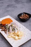 Peruvian ceviche seen in the foreground next to a portion of corn, the presentation of the dish is on a gray background. photo