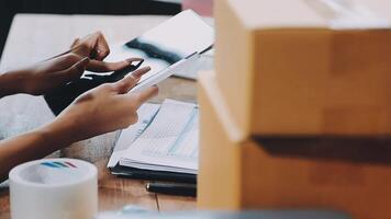 Startup small business SME, Entrepreneur owner African woman using smartphone or tablet taking receive and checking online purchase shopping order to preparing pack product box. video