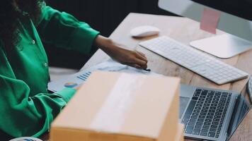 Startup small business SME, Entrepreneur owner African woman using smartphone or tablet taking receive and checking online purchase shopping order to preparing pack product box. video