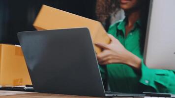 Startup small business SME, Entrepreneur owner African woman using smartphone or tablet taking receive and checking online purchase shopping order to preparing pack product box. video
