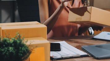 Startup small business SME, Entrepreneur owner African woman using smartphone or tablet taking receive and checking online purchase shopping order to preparing pack product box. video