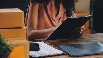 Startup small business SME, Entrepreneur owner African woman using smartphone or tablet taking receive and checking online purchase shopping order to preparing pack product box. video