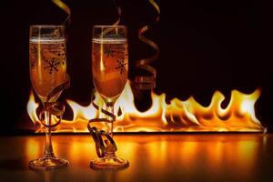 Two glasses of sparkling champagne with golden ribbons against the bokeh background of bright flames creating a cozy atmosphere of Christmas or New Year photo
