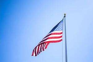 An american flag on a staff, waving in the wind with a clear blue sky and distant mountains as its backdrop, symbolizing usa independence day photo