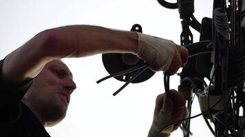 Skilled electrician fixes wires standing on ladder near high pole against blue sky on summer day backside view. Electrical service and mounting on the pole video