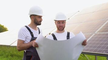 två arbetare ingenjörer talande med varje Övrig medan innehav en blå skriva ut med en stor sol- panel i bakgrund video