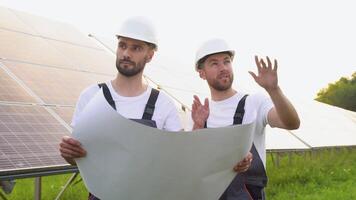 två arbetare ingenjörer talande med varje Övrig medan innehav en blå skriva ut med en stor sol- panel i bakgrund video
