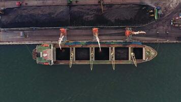 Top view of loading a cargo ship with coal using port cranes. Drone view video