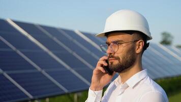 Confident engineer wearing safety hard hat, holding mobile phone, making a call. Engineer, worker, or architect working with Solar panel concept video