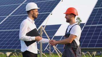 Two engineers boss and subordinate shaking hands after discussion on background of photovoltaic solar panels video