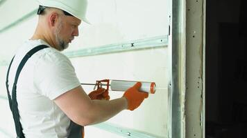 Worker in uniform is applying polyurethane foam to fill gap on drywall wall video
