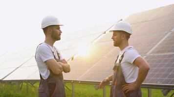 Two workers engineers in helmet and overalls shaking hands after discussion on background of photovoltaic solar panels video