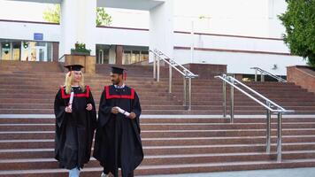 Happy multiracial graduates are walking the stairs in university in mantles with diplomas in hand video
