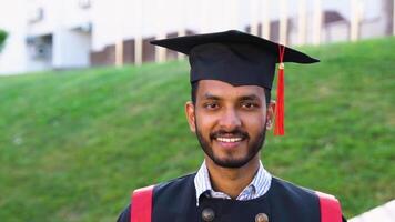 Smiling graduate indian student in graduations gown and hat walking with diploma in campus video