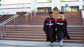 Happy multiracial graduates are walking the stairs in university in mantles with diplomas in hand video